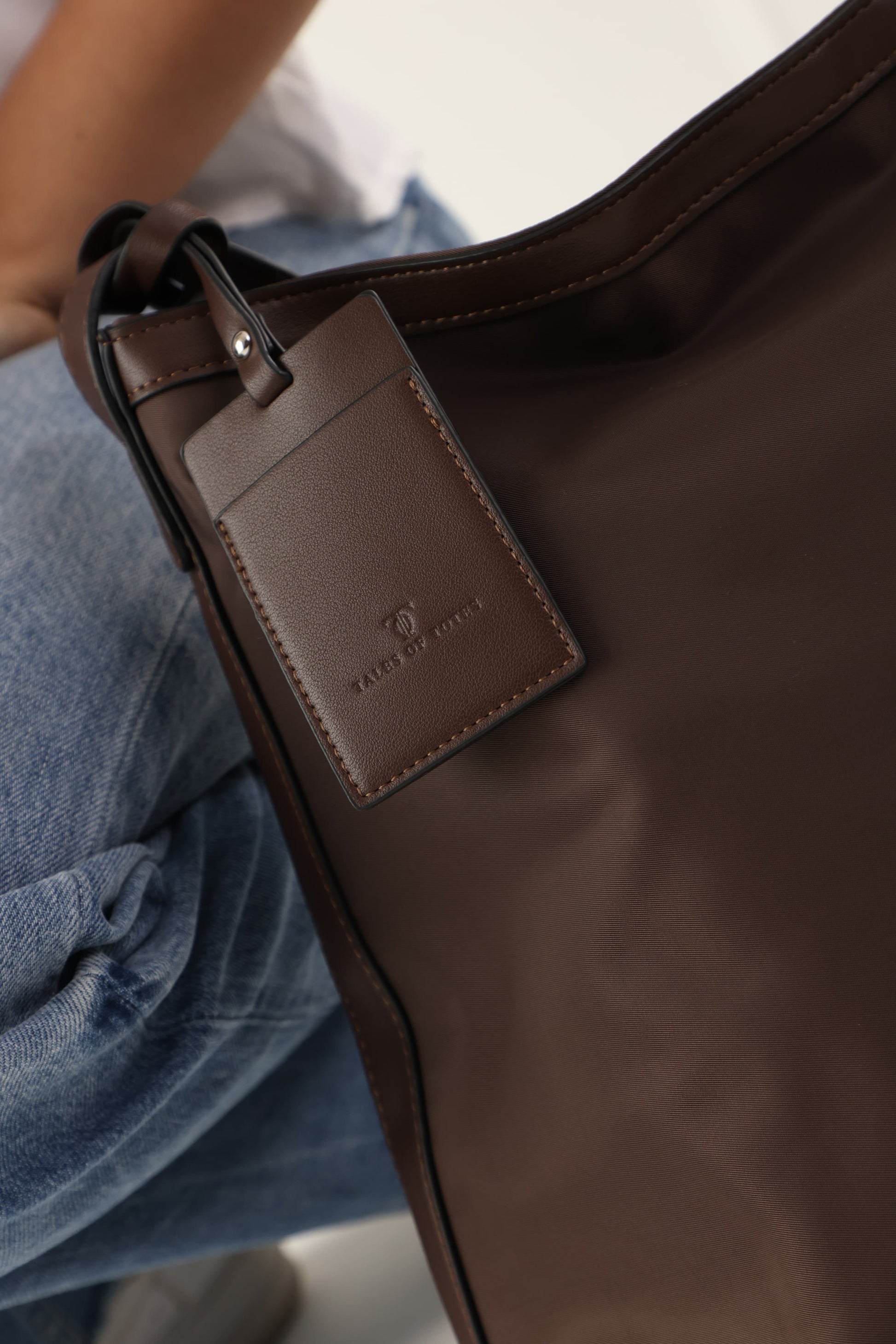 "Minimalist shoulder bag with a structured silhouette, single top strap, and attached tag detail – designed for effortless everyday style. Compact yet spacious enough for daily essentials, perfect for work, brunch, or casual wear. A premium fashion accessory from Tales of Totes, ideal for Indian shoppers seeking elegant, functional handbags beyond standard tote designs."
