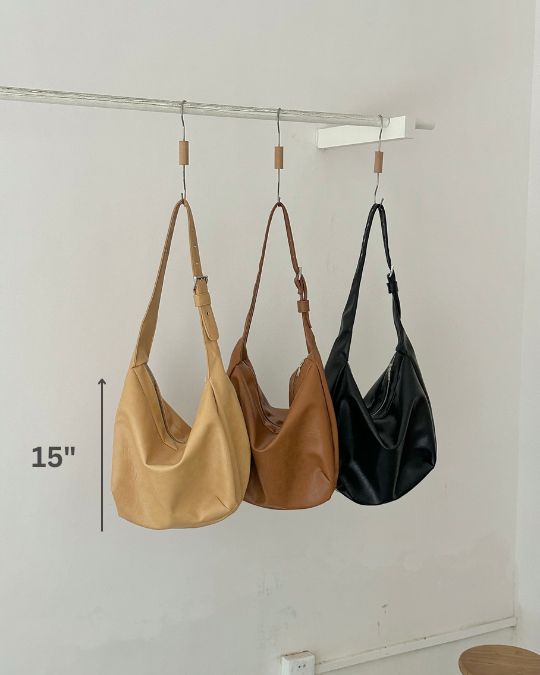 Three handbags in beige, brown, and black hanging on a rack with a measurement label.