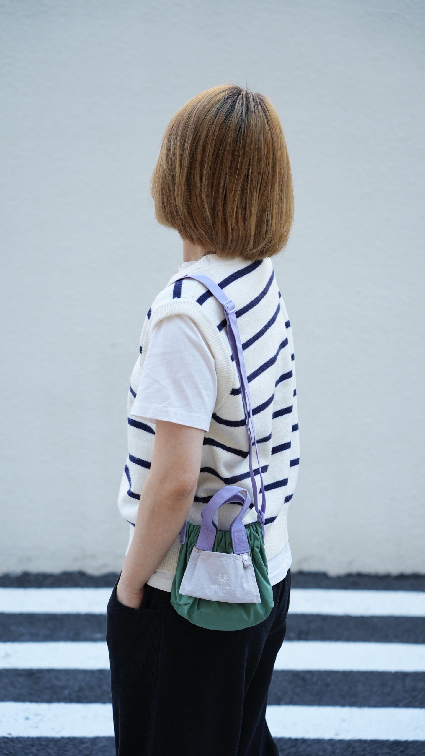 Person with a striped shirt and green backpack standing on a crosswalk.