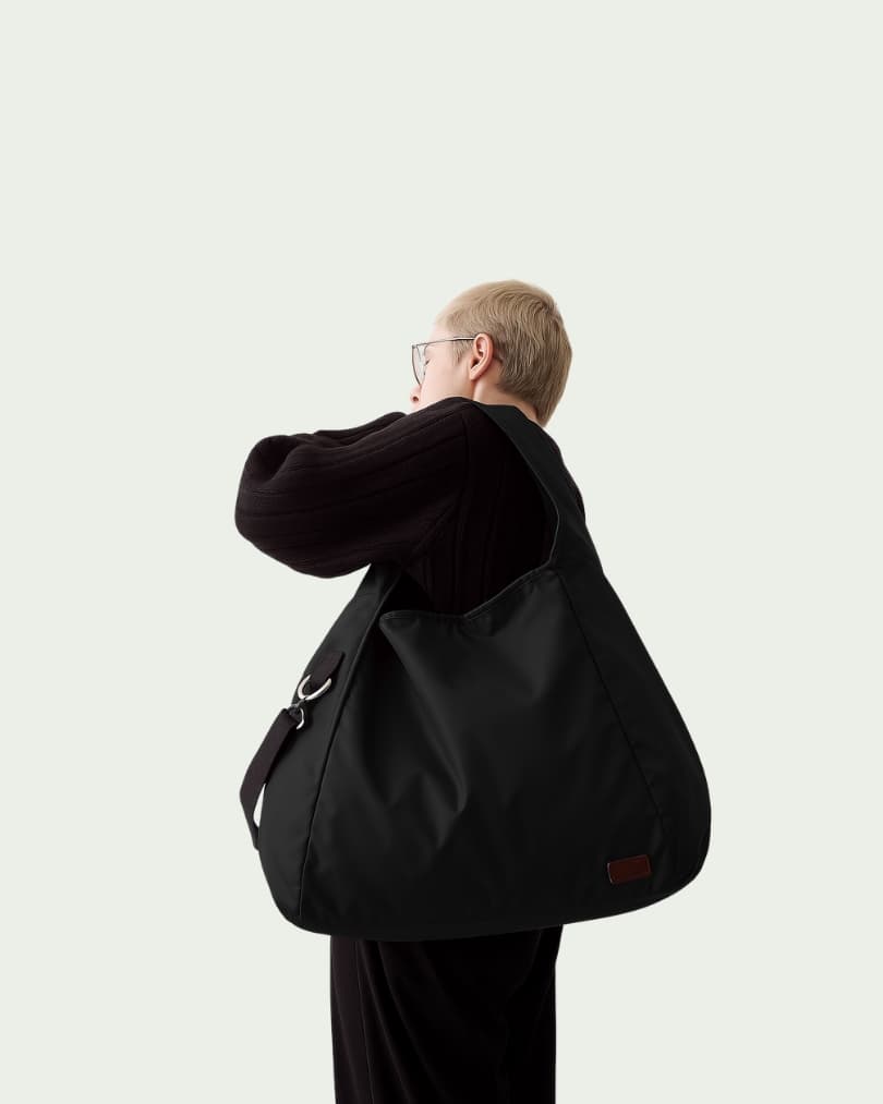 Minimalist black tote bag with a padded top handle, detachable crossbody strap, and front zipper pocket – made from water-resistant fabric for everyday functionality. Lightweight yet spacious, ideal for travel, office, gym, or casual use. A sleek and versatile design by Tales of Totes, offering modern utility and elevated style for Indian shoppers."