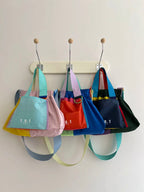 Four colorful T.O.T canvas tote bags in pastel and bright colors hanging from a cream-colored peg rail on a white wall.