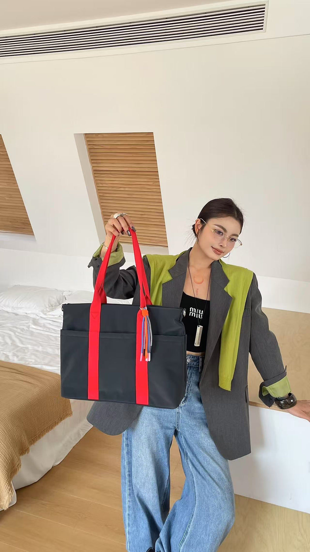 Person holding a black bag with red straps in a bedroom setting