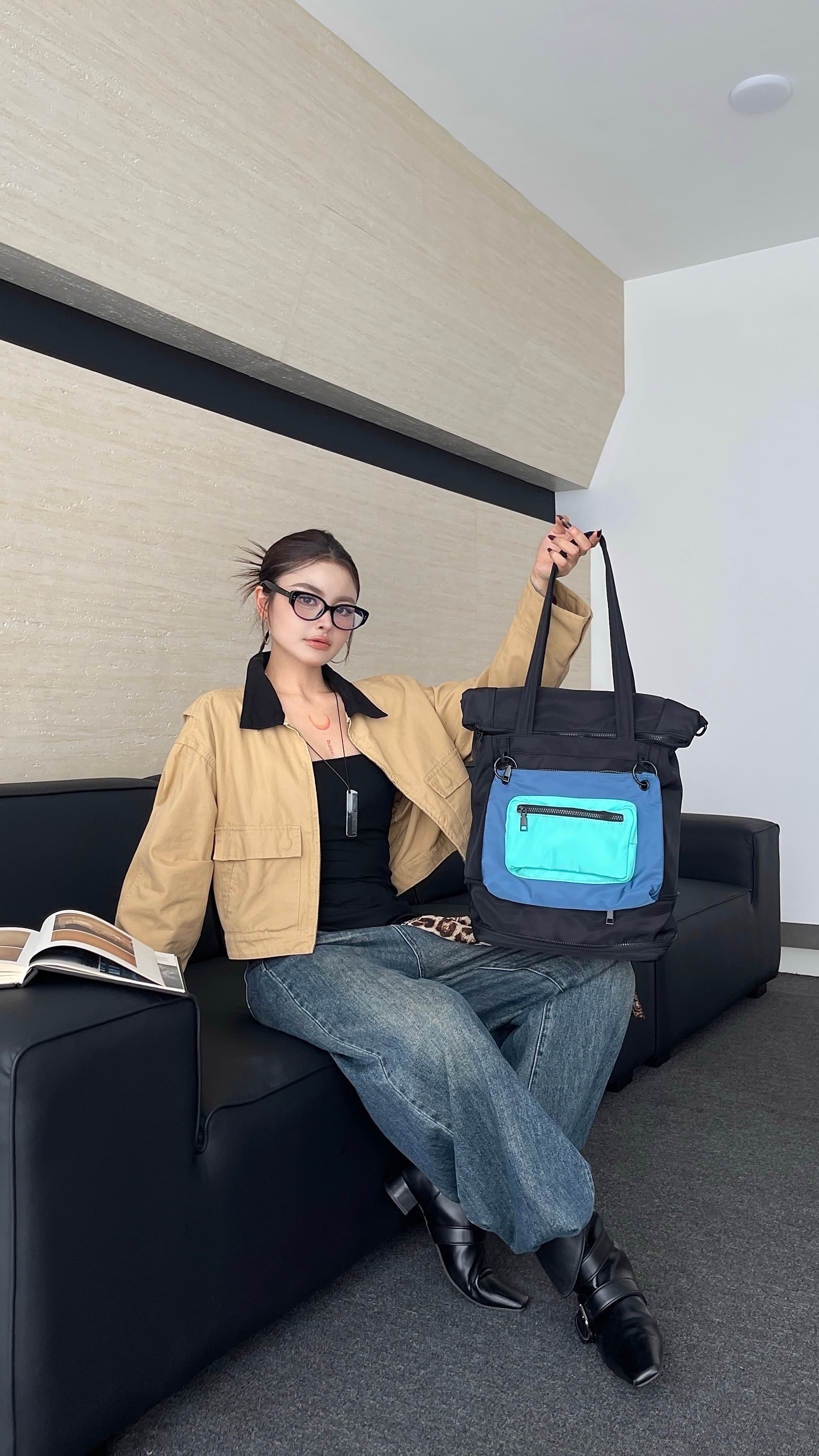 Person sitting on a couch holding a blue bag with a green screen, in a room with a neutral color scheme.