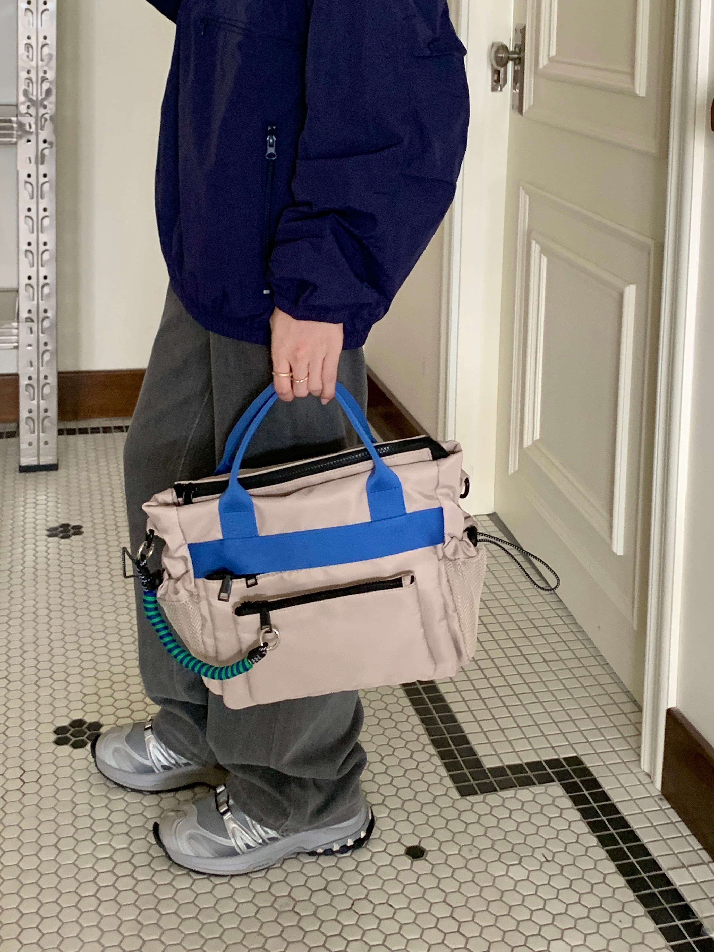 Person holding a beige bag with blue handles in a room with tiled floor and white door.