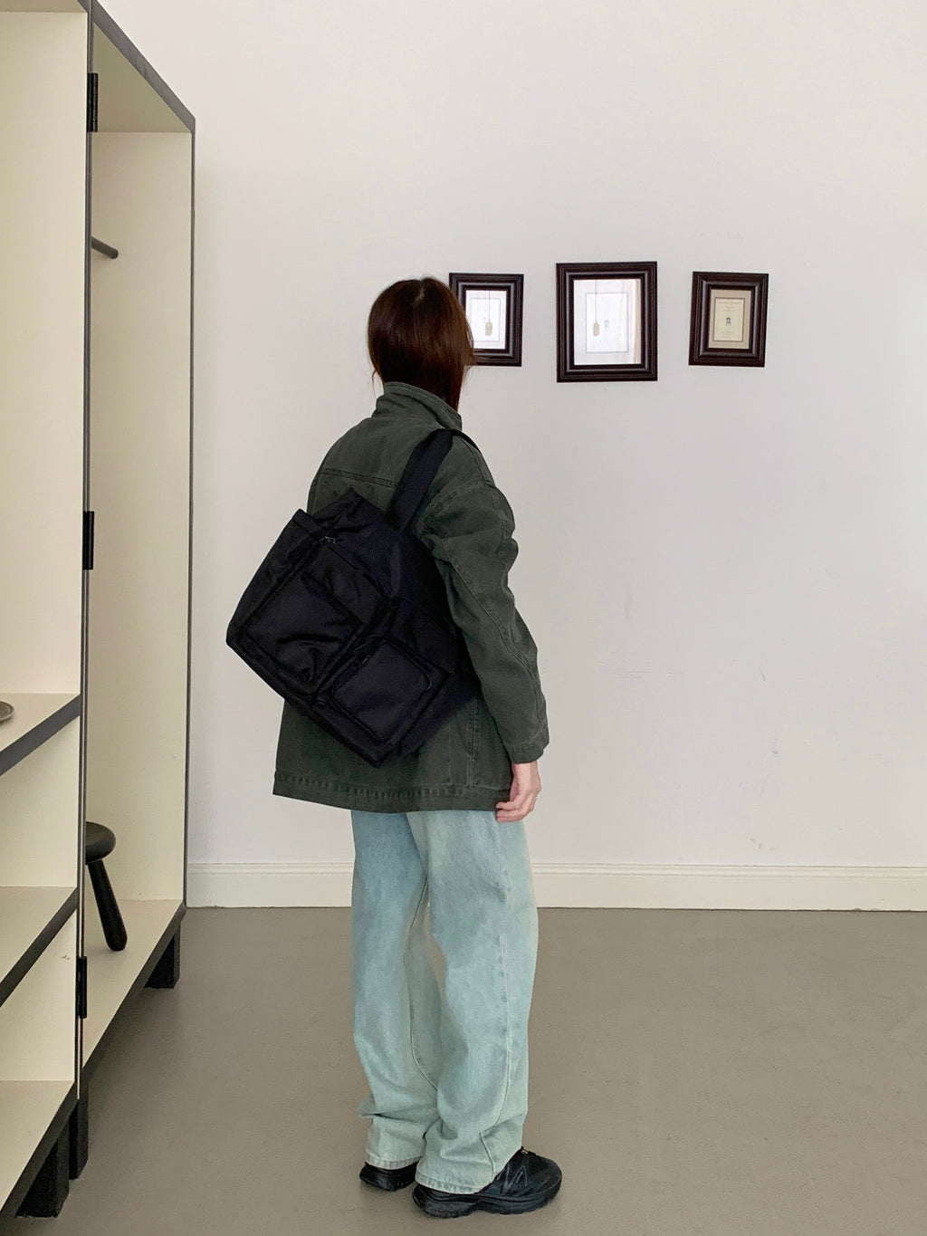 Person wearing a green coat and light blue jeans, carrying a black backpack, standing in an art gallery.