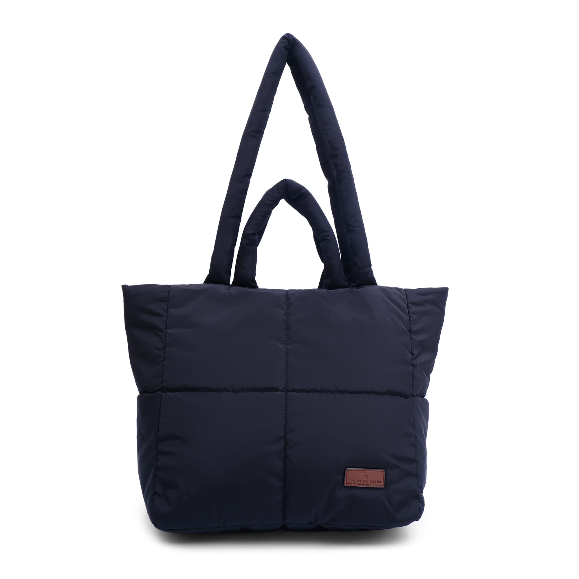 black tote bag with a brown patch on a white background "Minimalist shoulder bag with a structured silhouette, single top strap, and attached tag detail – designed for effortless everyday style. Compact yet spacious enough for daily essentials, perfect for work, brunch, or casual wear. A premium fashion accessory from Tales of Totes, ideal for Indian shoppers seeking elegant, functional handbags beyond standard tote designs."
