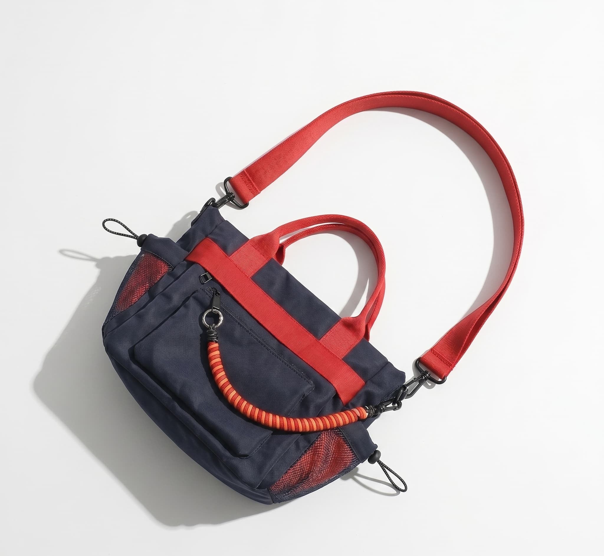 Navy and red handbag with a coiled orange rope on a light gray background