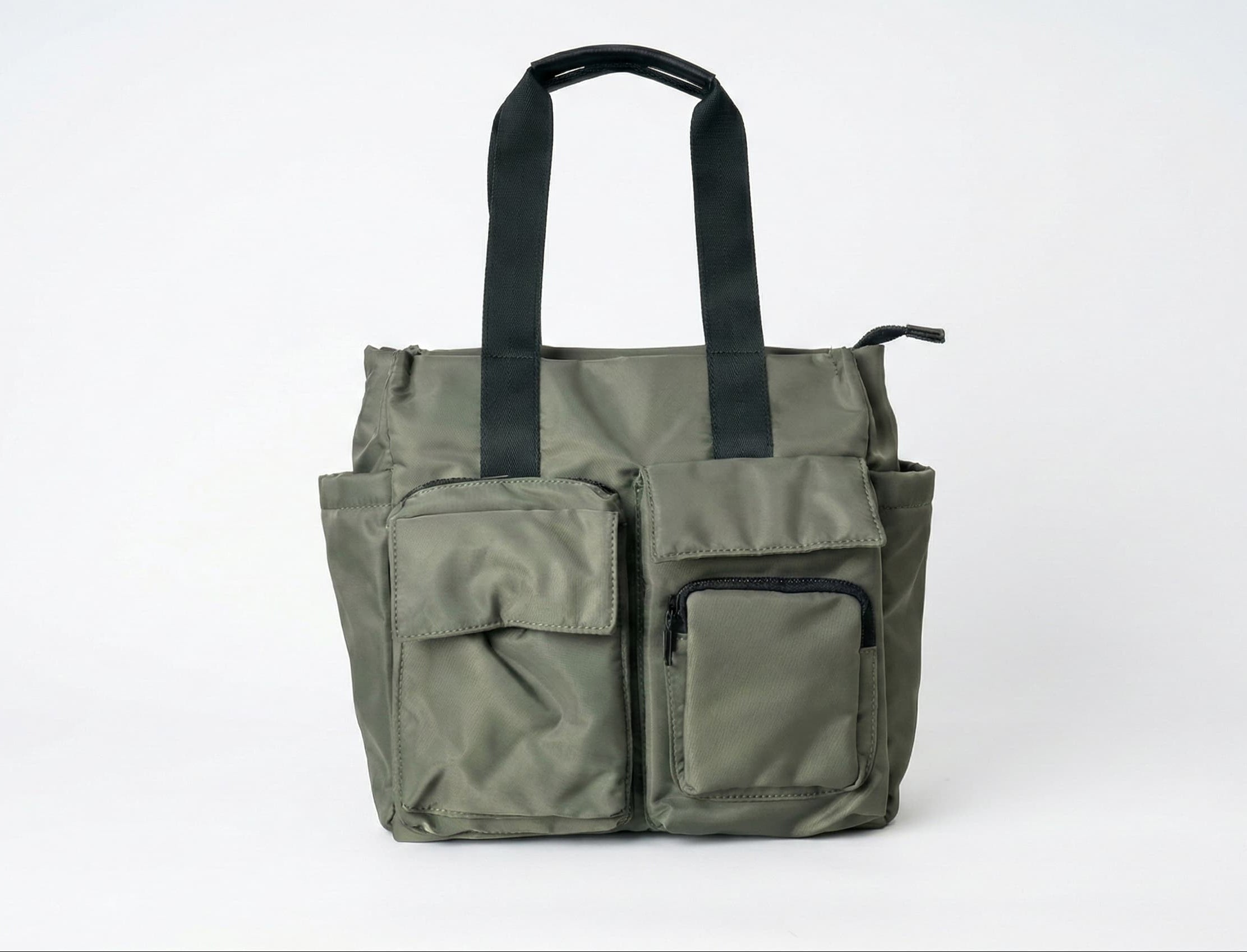 Green tote bag with multiple pockets and black straps on a white background Bag 004 olive green streetwear utility tote bag India with oversized structured design and durable canvas material, unisex urban carry bag for daily use, travel and campus life, military inspired minimal street aesthetic competing with Urban Monkey and H&M street collection, heavy duty shoulder straps with reinforced stitching, functional tote bag for laptop and essentials, modern Indian hype street fashion accessory designed for du