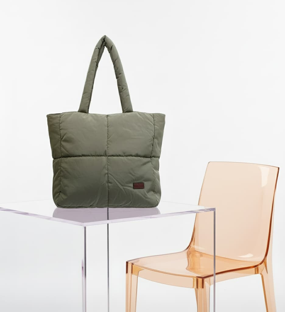 Green puffer bag on a clear table with a transparent orange chair in the background