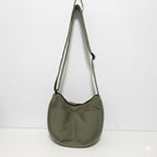 Green shoulder bag hanging against a white background.Trendy emerald green crescent half-moon shoulder bag for women, durable canvas, versatile for daily use, ethnic wear, and casual outings in India. This stylish sling bag offers a modern minimalist design, spacious interior, functioning as a chic carryall or small hobo tote.