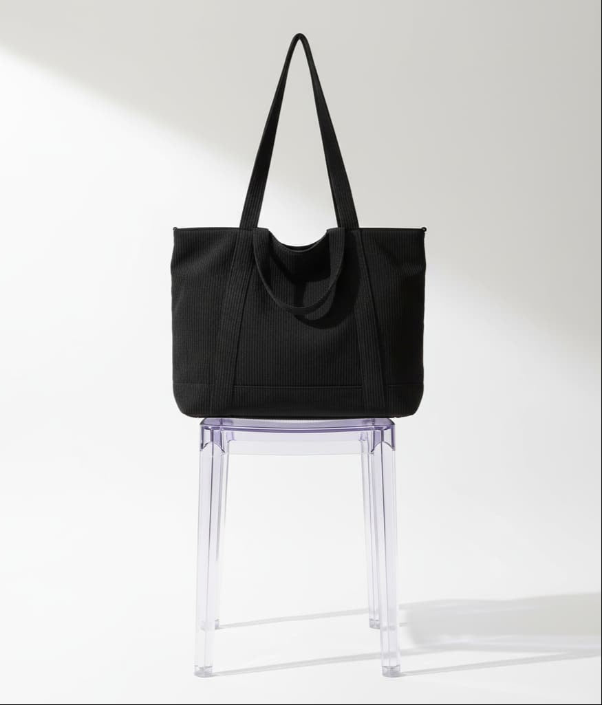 Black tote bag on a clear plastic stool against a white backgroundTrendy corduroy tote bag with dual handles and adjustable crossbody strap – soft-textured, oversized, and perfect for college, shopping, or everyday carry. Lightweight yet spacious, offering a casual streetwear aesthetic. A fashionable alternative from Tales of Totes – elevating Indian accessory trends beyond Zouk, Chumbak, and DailyObjects."
