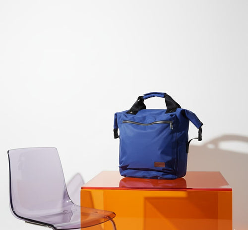 Blue backpack on an orange cube with a clear chair against a white background