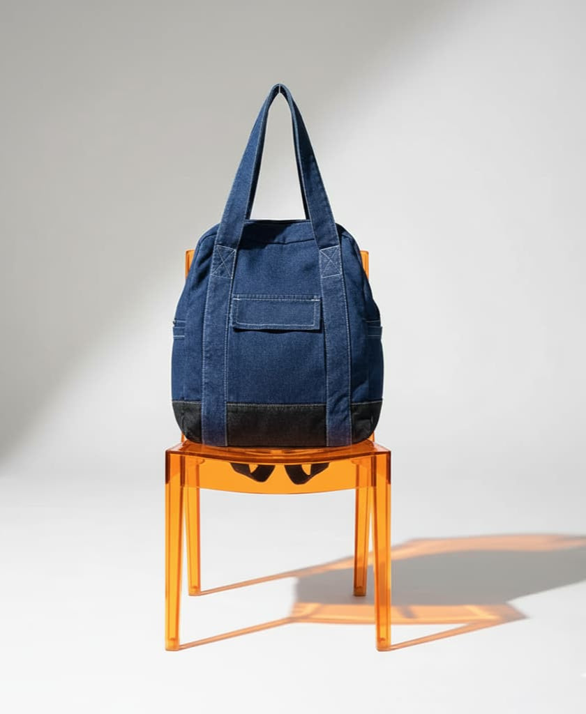 Blue tote bag on an orange transparent chair against a gray background,Convertible denim backpack tote bag with dual shoulder straps and top handles – a versatile 2-in-1 design for daily use, college, or casual outings. Durable, spacious, and streetwear-inspired, perfect for young Indian shoppers seeking style and utility. Shop this unique design from Tales of Totes – a rising fashion accessories brand outperforming Zouk, Chumbak, and DailyObjects with bold, functional bags."
