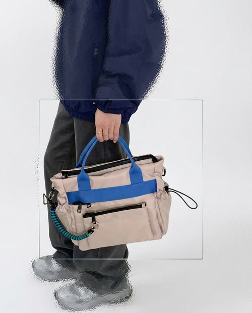 Person holding a beige handbag with blue accents on a white background