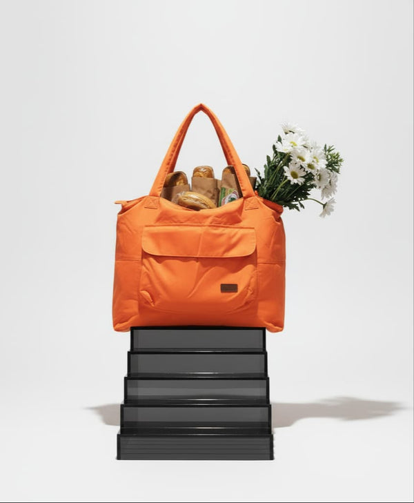 Orange tote bag with groceries on a white backgroundPerson holding an orange reusable shopping bag filled with groceries in a supermarket.Person wearing a black coat and holding an orange bag on a white background,Gray tote bag with a hand reaching in to place a bottle, on a white backgroundLightweight nylon tote bag with a padded handle design and front flap pocket – perfect for everyday errands, gym, shopping, or casual travel. Spacious, foldable, and easy to carry with a functional structure that balance