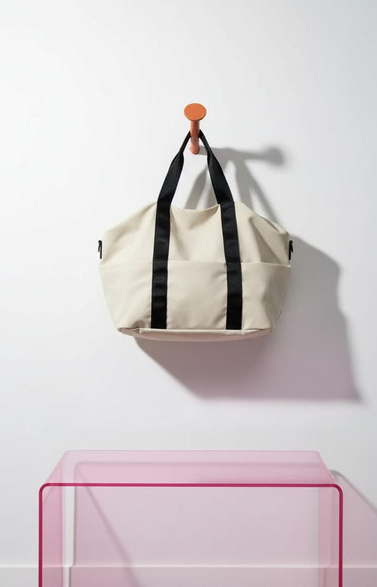 Beige bag with black straps hanging on a white wall with a pink transparent table in the foreground.Beige bag with black straps and measurements on a white backgroundA unisex duffel tote bag with a sleek, minimal design featuring two vertical straps, dual carry handles, an adjustable shoulder strap, and side pockets. Spacious enough for travel or daily use, crafted from durable, water-resistant material with a zippered top closure. Ideal for college, gym, or casual outings.

