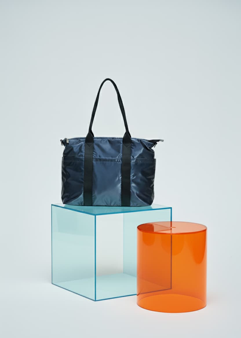 Blue tote bag on a clear blue cube with an orange cylindrical object on a light gray background