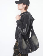 Person wearing a black hoodie with a unique design, holding a black studded bag against a white background.