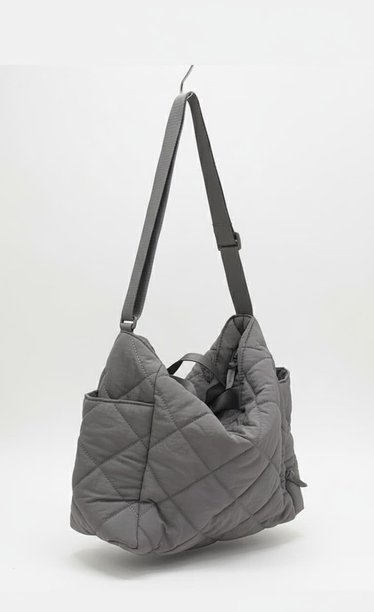 Gray quilted handbag with a strap on a white background,Quilted tote bag with a luxe padded finish – soft, stylish, and built for everyday use. Made for Indian shoppers who love the look of designer bags without the heavy price tag. Spacious enough for laptops and daily essentials. Tales of Totes offers a premium alternative to Miraggio, Zouk, and Lavie – where quilted fashion meets function."