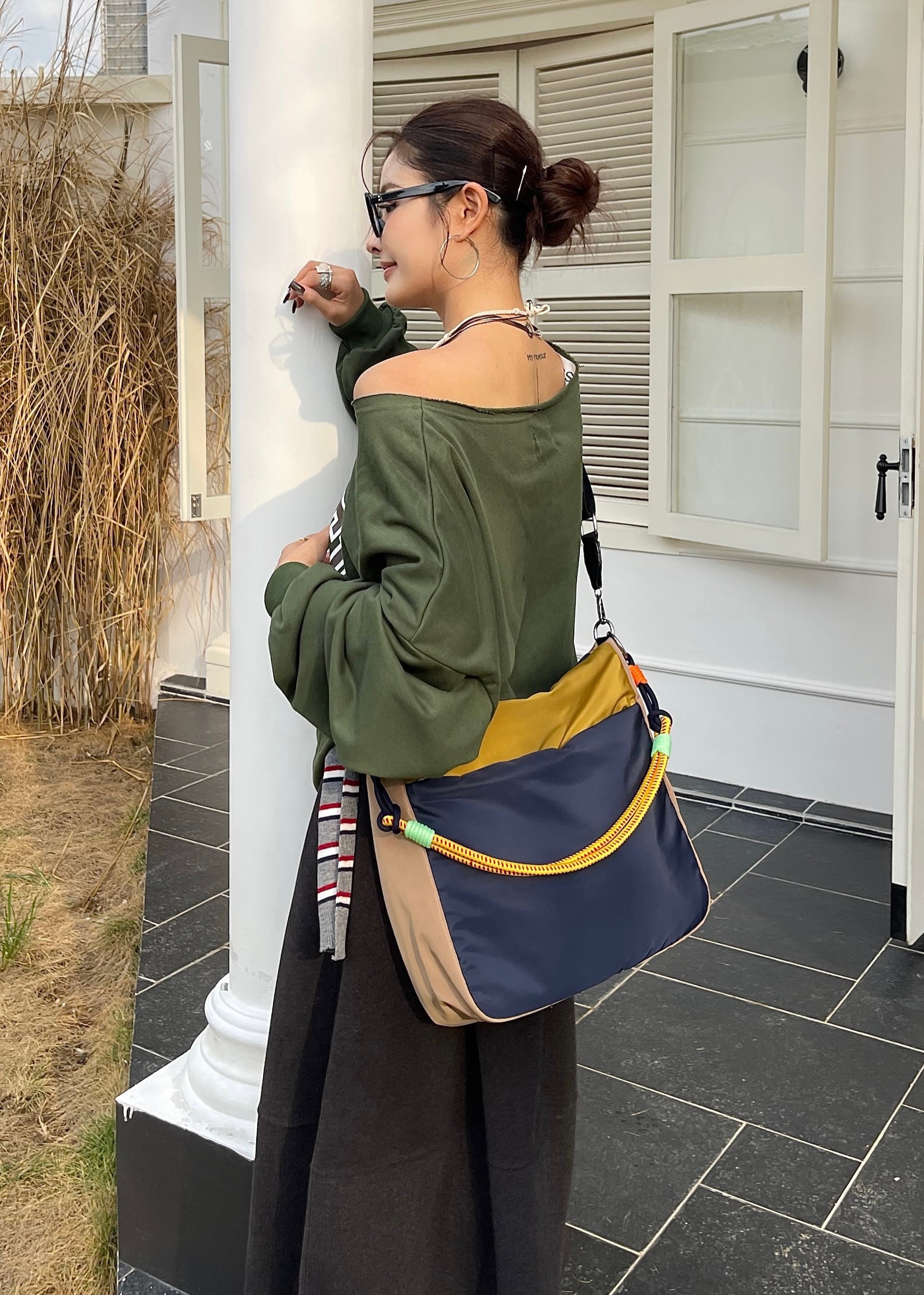 Woman standing outside a house holding a colorful bag Multi-pocket travel tote bag with 20-litre capacity and compact dimensions (35 x 35 x 10 cm), featuring a wide adjustable strap and color-blocked utility design. Lightweight, durable, and ideal for travel, college, or daily use. A high-performance everyday essential from Tales of Totes – built for comfort, style, and smart organization in India’s fast-paced lifestyle."
