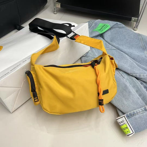 Yellow waist bag on a light gray surface with jeans and a box in the background,Mini utility tote bag 33x22x14 cm with multiple pockets, zip closure, and water-resistant nylon material. Everyday carry tote for men and women, ideal for office, travel, and casual use in India. Alternative to Muji tote, Decathlon utility bag, and Wildcraft crossbody. Features bright orange inner lining and durable adjustable strap.