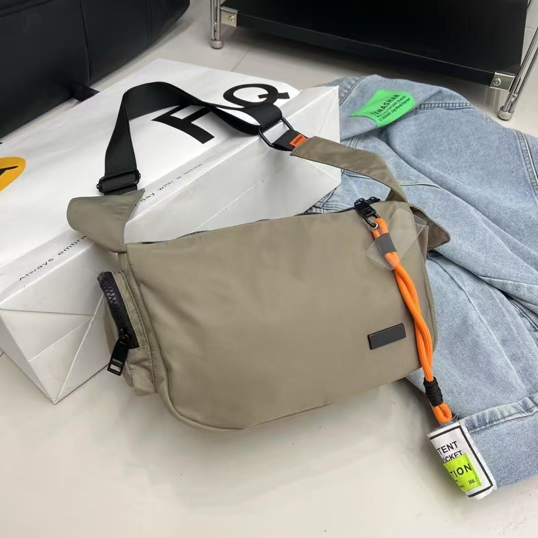 Beige shoulder bag with orange strap on a light surface with jeans and a box in the background Mini utility tote bag 33x22x14 cm with multiple pockets, zip closure, and water-resistant nylon material. Everyday carry tote for men and women, ideal for office, travel, and casual use in India. Alternative to Muji tote, Decathlon utility bag, and Wildcraft crossbody. Features bright orange inner lining and durable adjustable strap.
