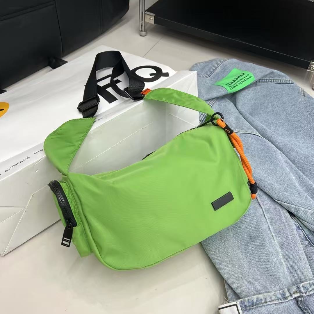 Green shoulder bag on a white surface with jeans and a magazine in the background,Mini utility tote bag 33x22x14 cm with multiple pockets, zip closure, and water-resistant nylon material. Everyday carry tote for men and women, ideal for office, travel, and casual use in India. Alternative to Muji tote, Decathlon utility bag, and Wildcraft crossbody. Features bright orange inner lining and durable adjustable strap.