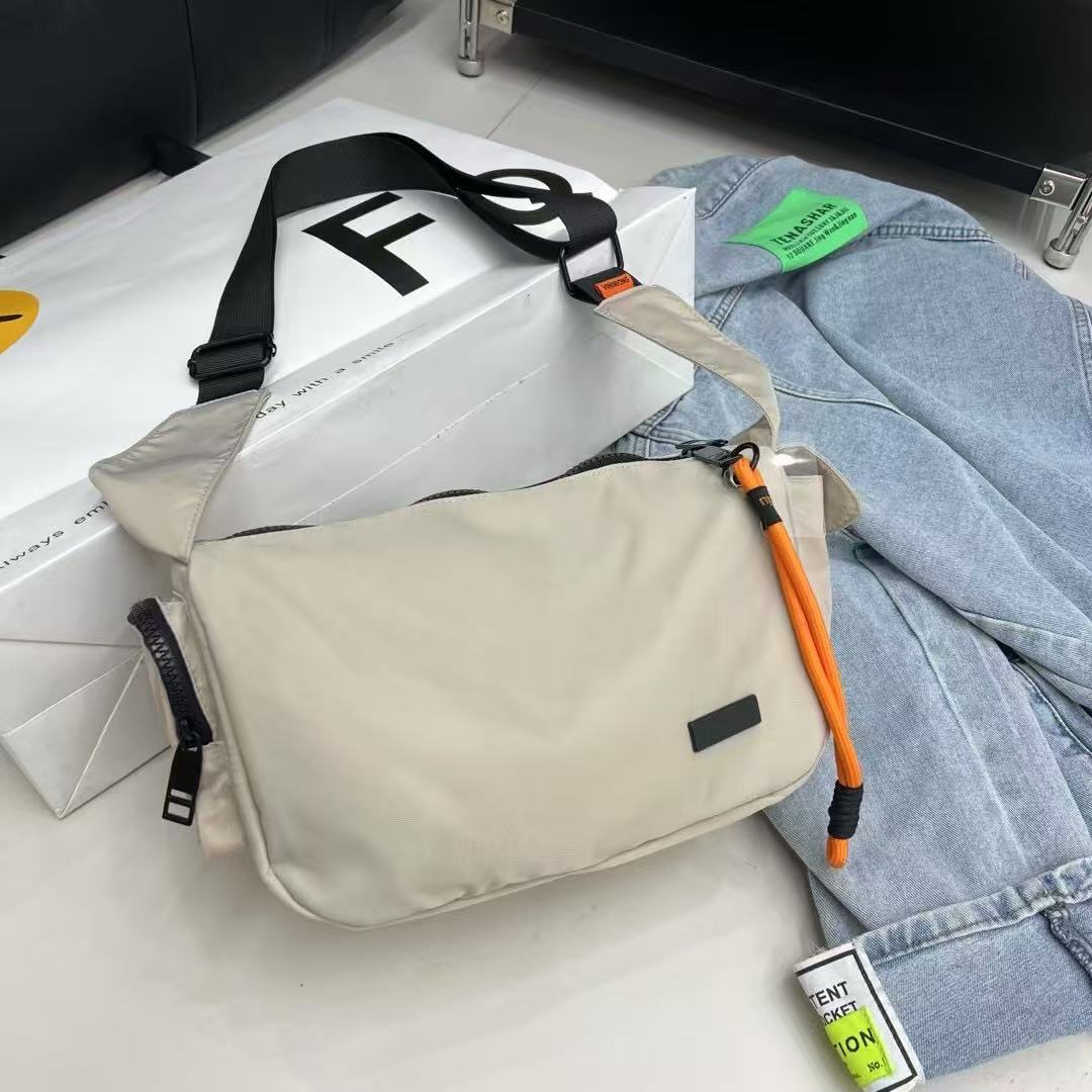 Beige crossbody bag with orange accents on a white surface with jeans and a box in the backgroundMini utility tote bag 33x22x14 cm with multiple pockets, zip closure, and water-resistant nylon material. Everyday carry tote for men and women, ideal for office, travel, and casual use in India. Alternative to Muji tote, Decathlon utility bag, and Wildcraft crossbody. Features bright orange inner lining and durable adjustable strap.