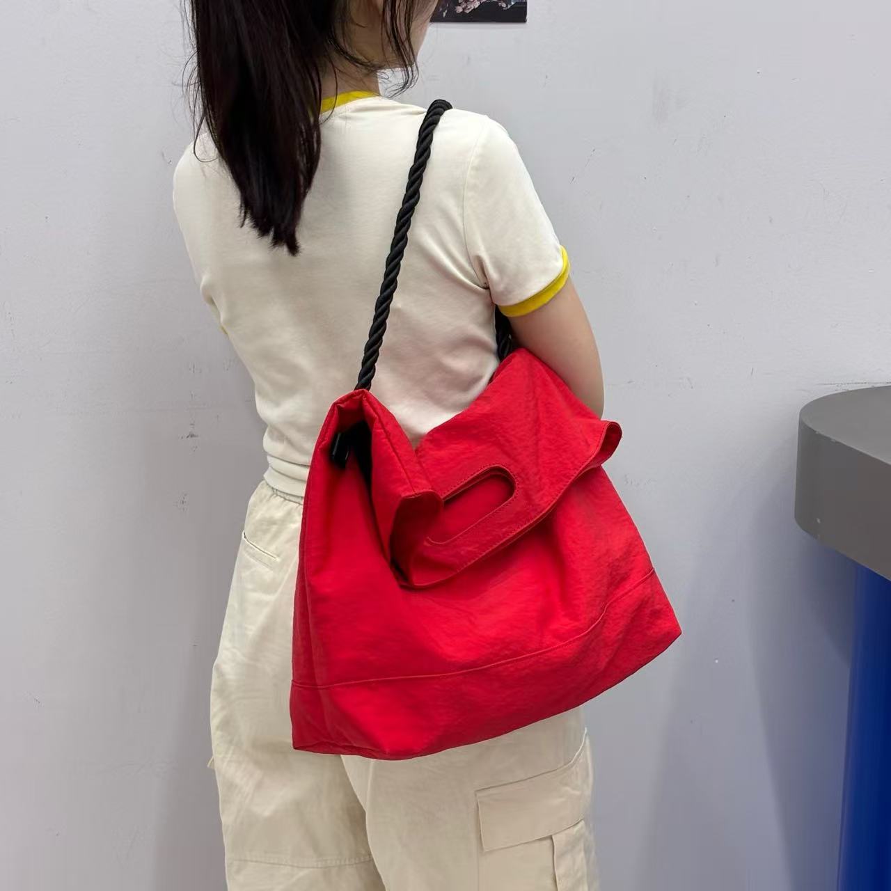 Person holding a red bag against a plain background,High-quality red tote bag for women and girls from a new Indian fashion brand. Features a unique top-fold flap design and sturdy braided black rope handles. Perfect for carrying laptops and essentials, making it a stylish and functional bag for office, college, or casual outings in India. A chic and trending design for the modern Indian woman, available online with free shipping.