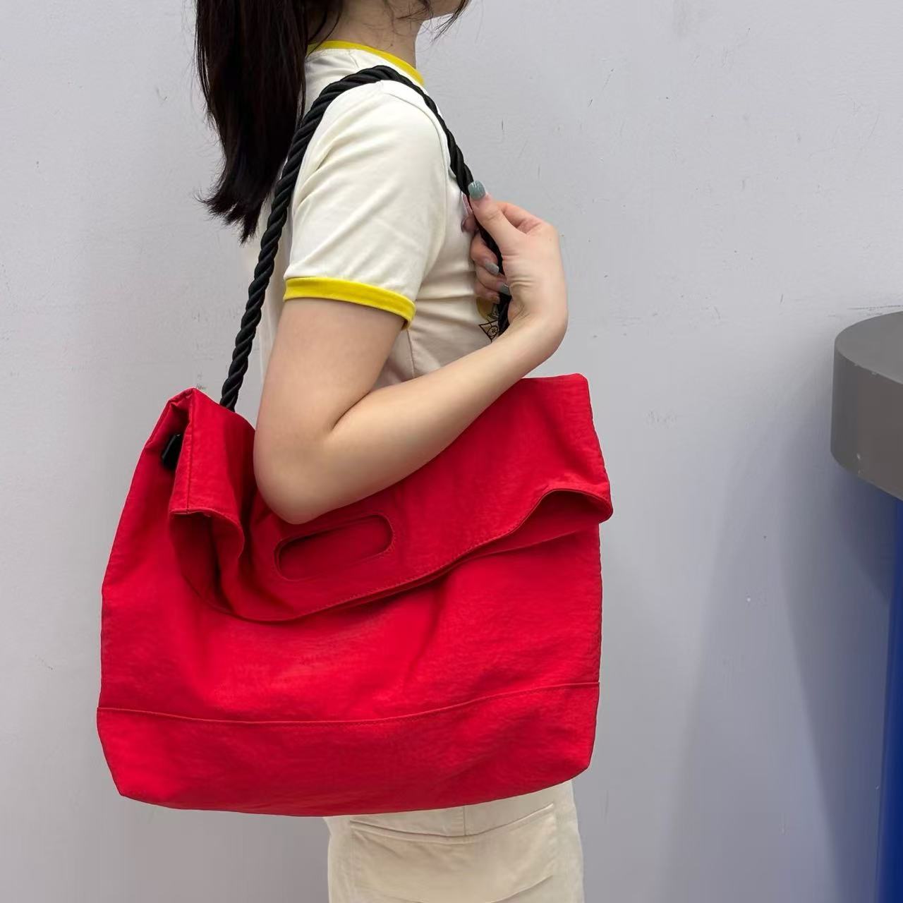 Person holding a red bag against a plain background,High-quality red tote bag for women and girls from a new Indian fashion brand. Features a unique top-fold flap design and sturdy braided black rope handles. Perfect for carrying laptops and essentials, making it a stylish and functional bag for office, college, or casual outings in India. A chic and trending design for the modern Indian woman, available online with free shipping.