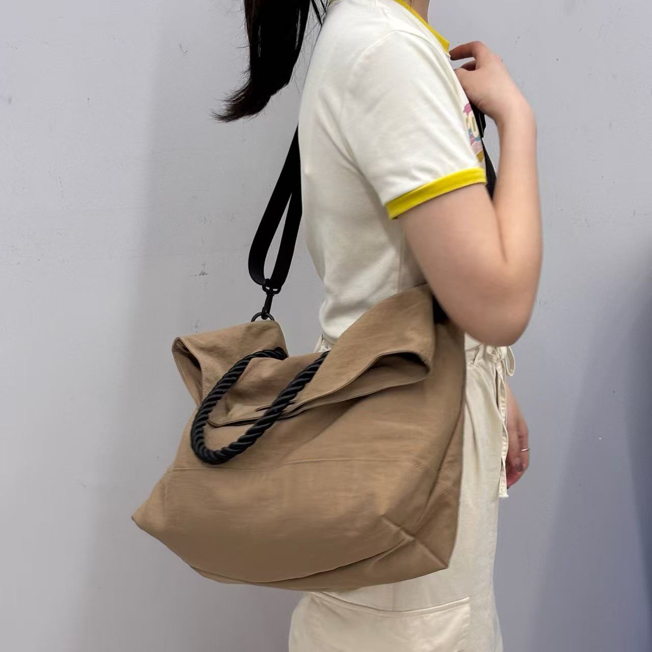 Person holding a beige bag against a plain background,High-quality red tote bag for women and girls from a new Indian fashion brand. Features a unique top-fold flap design and sturdy braided black rope handles. Perfect for carrying laptops and essentials, making it a stylish and functional bag for office, college, or casual outings in India. A chic and trending design for the modern Indian woman, available online with free shipping.