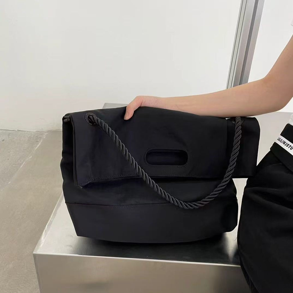 Black handbag with a rope handle held by a person on a white surface.,High-quality red tote bag for women and girls from a new Indian fashion brand. Features a unique top-fold flap design and sturdy braided black rope handles. Perfect for carrying laptops and essentials, making it a stylish and functional bag for office, college, or casual outings in India. A chic and trending design for the modern Indian woman, available online with free shipping.