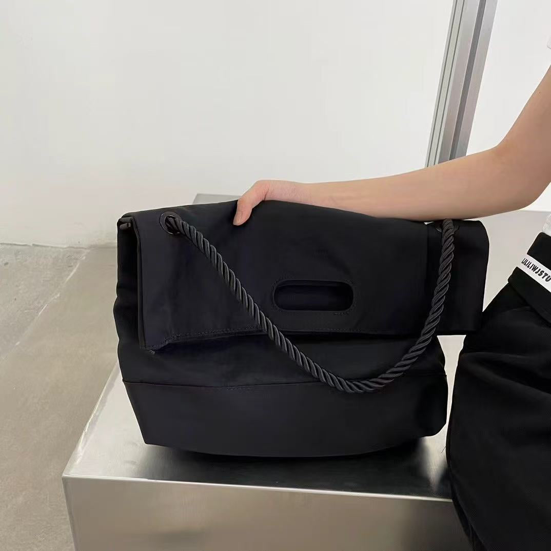 Black handbag with a rope handle held by a person on a white surface.,High-quality red tote bag for women and girls from a new Indian fashion brand. Features a unique top-fold flap design and sturdy braided black rope handles. Perfect for carrying laptops and essentials, making it a stylish and functional bag for office, college, or casual outings in India. A chic and trending design for the modern Indian woman, available online with free shipping.