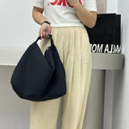Person holding a black bag wearing a white t-shirt with red text and beige pants.Convertible nylon tote bag with detachable crossbody strap, zippered front pocket, and main compartment. Available in olive green, black, and beige.