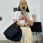 Person wearing a white t-shirt with red text, beige cap, and holding a black bag.Convertible nylon tote bag with detachable crossbody strap, zippered front pocket, and main compartment. Available in olive green, black, and beige.