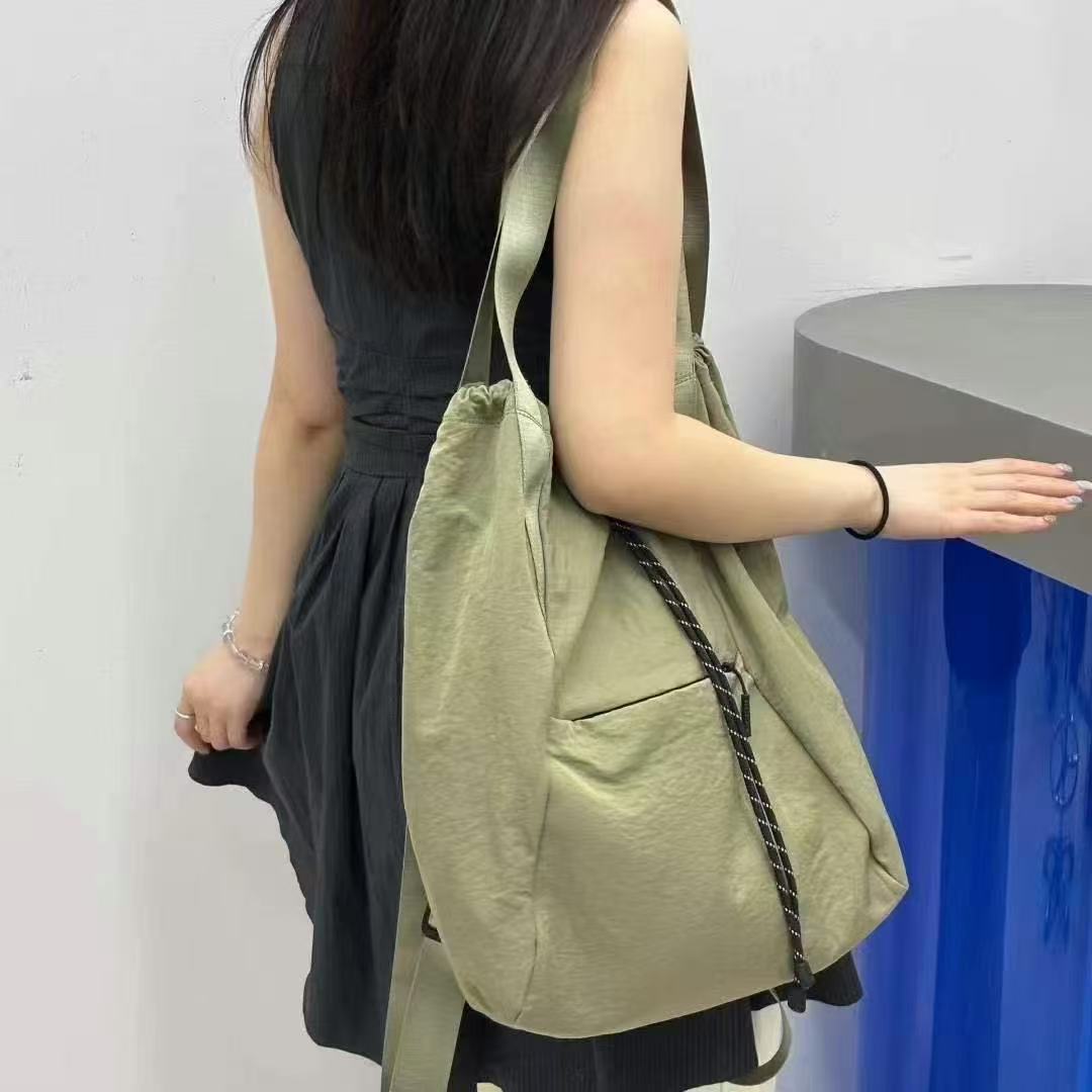 Woman holding a green tote bag against a plain background,"Stylish khaki drawstring tote bag with multiple compartments and adjustable straps, perfect for daily use, shopping, and travel in India. Features include a secure zippered pocket, spacious main compartment, and comfortable shoulder straps. Ideal for fashion-conscious individuals seeking a versatile and trendy bag."