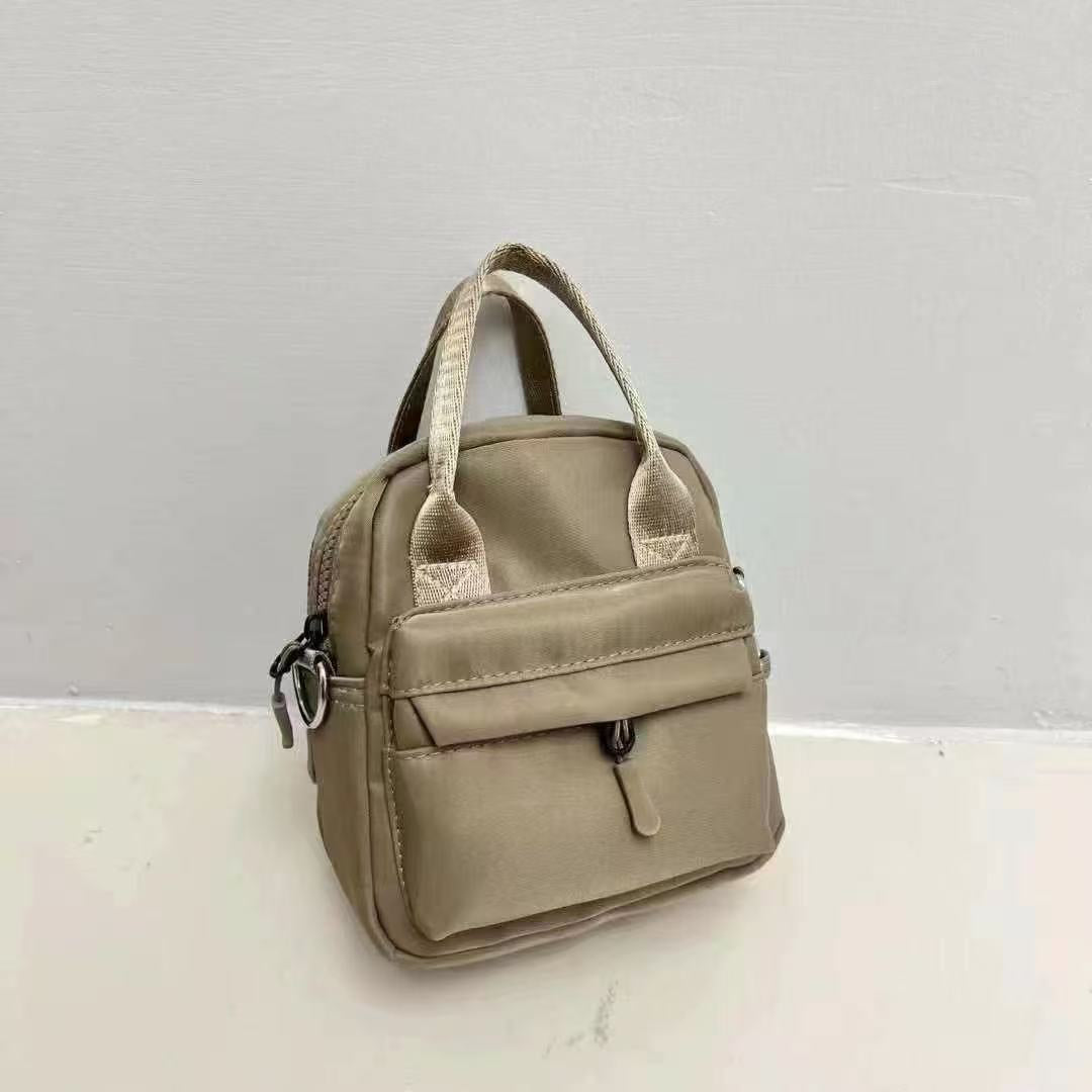 Beige handbag on a white surface with a light gray background,A high-fashion shot of a woman in a black skirt and white shirt, holding a stylish, minimalist brown bag. The image is professionally lit in a studio against a clean white background, with a strong focus on the bag's sleek design and texture. The photo emphasizes a sophisticated and modern aesthetic, perfect for luxury or premium lifestyle brands.