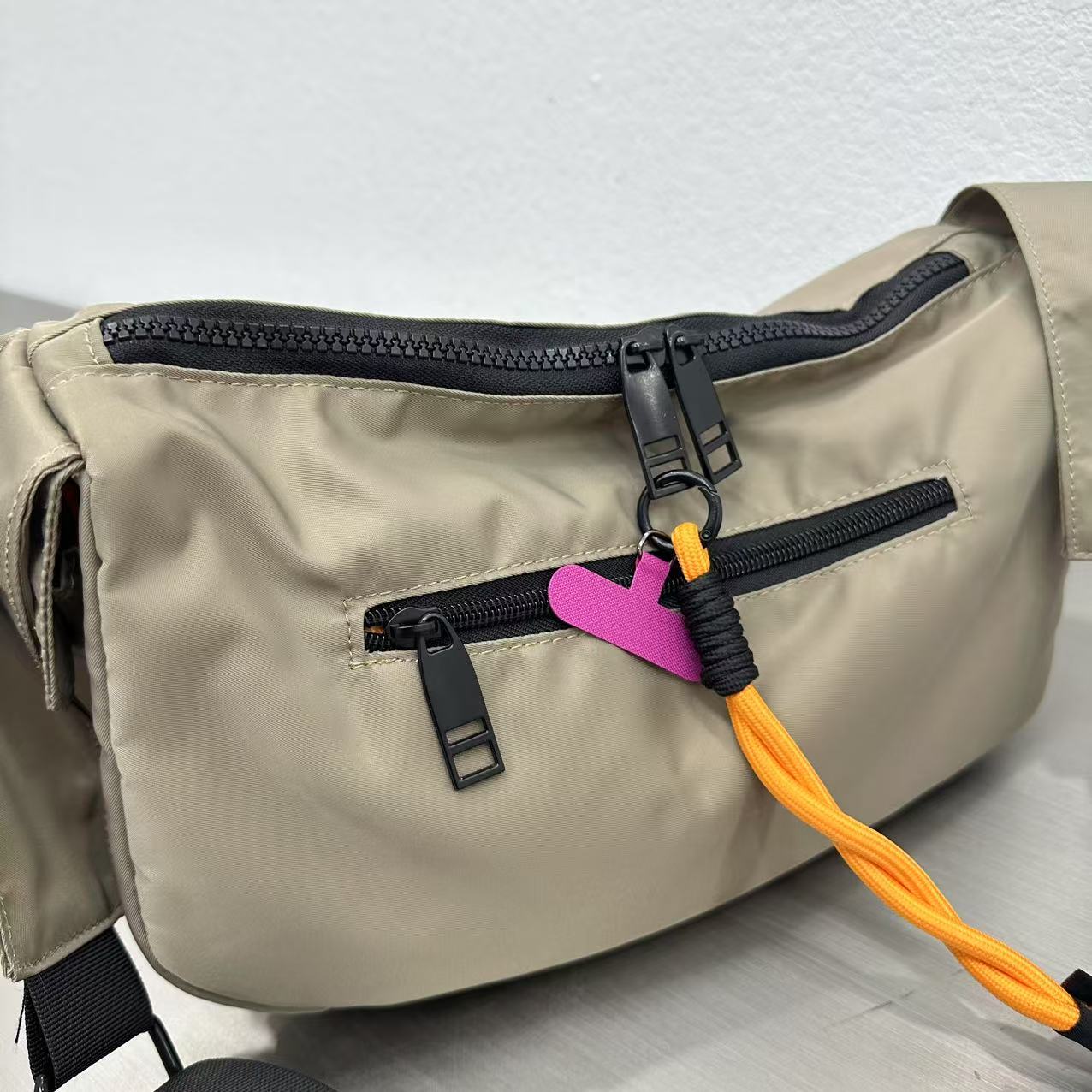 Beige bag with a black zipper and colorful tag on a light gray background,Mini utility tote bag 33x22x14 cm with multiple pockets, zip closure, and water-resistant nylon material. Everyday carry tote for men and women, ideal for office, travel, and casual use in India. Alternative to Muji tote, Decathlon utility bag, and Wildcraft crossbody. Features bright orange inner lining and durable adjustable strap.