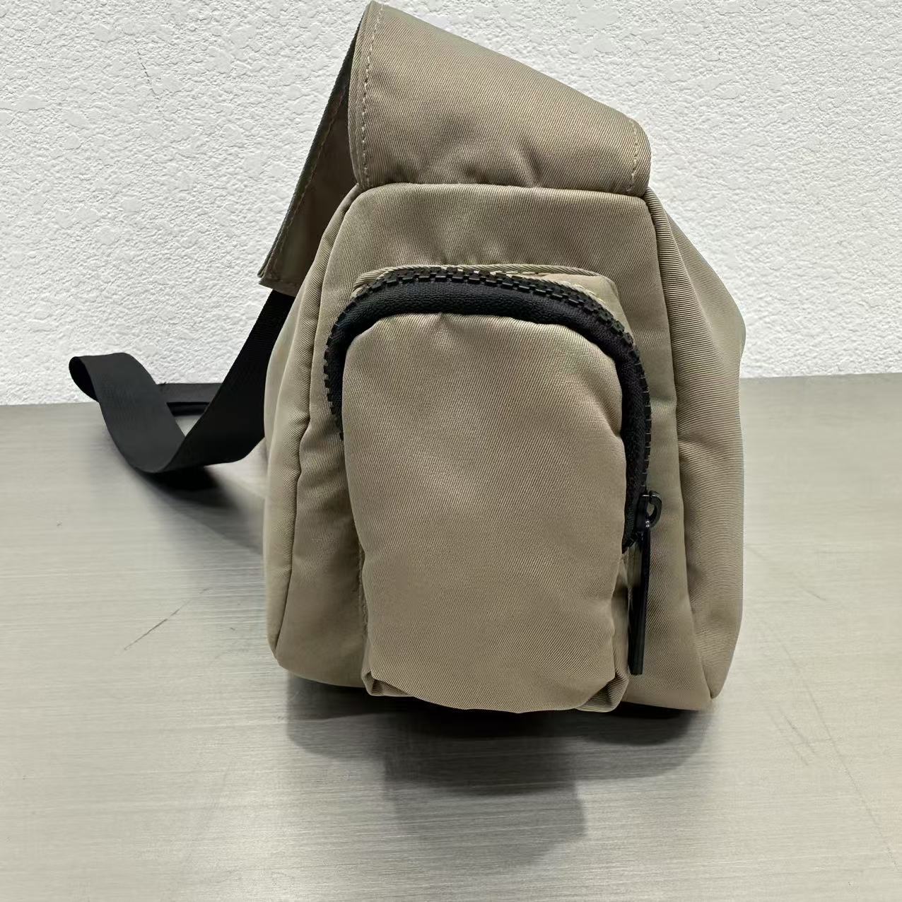 Beige sling bag with a black zipper on a light gray surface.Mini utility tote bag 33x22x14 cm with multiple pockets, zip closure, and water-resistant nylon material. Everyday carry tote for men and women, ideal for office, travel, and casual use in India. Alternative to Muji tote, Decathlon utility bag, and Wildcraft crossbody. Features bright orange inner lining and durable adjustable strap.
