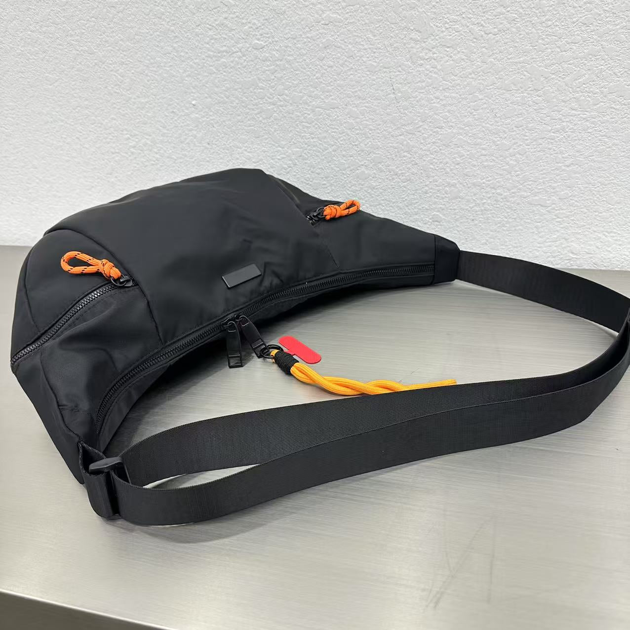 Black bag with a strap on a light gray surfaceWaterproof tote bag with a durable exterior and a bright orange interior. Features an adjustable strap and multiple pockets for organization. Ideal for travel, gym, or daily use in India.