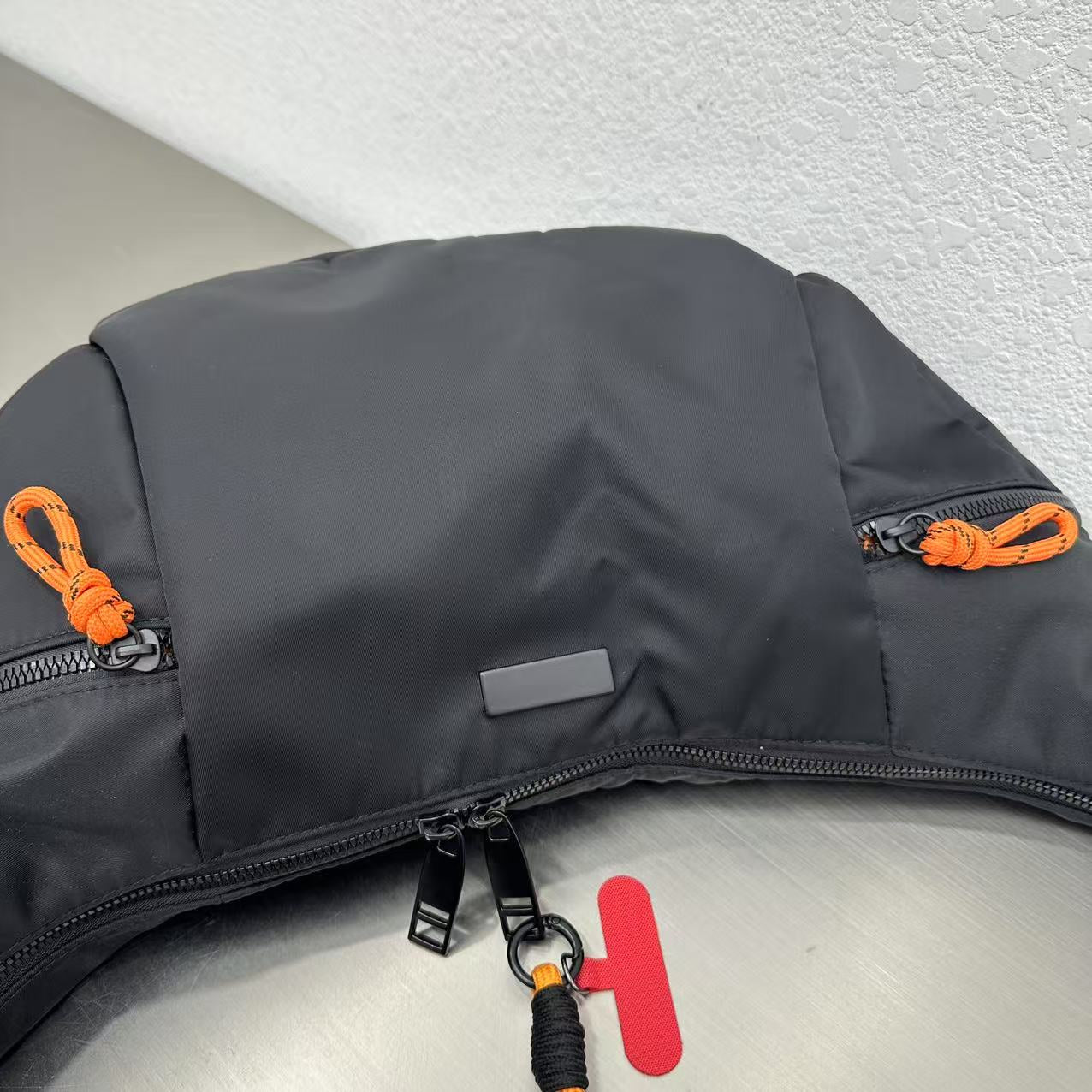 Gray bag with orange and black zippers on a light gray backgroundWaterproof tote bag with a durable exterior and a bright orange interior. Features an adjustable strap and multiple pockets for organization. Ideal for travel, gym, or daily use in India.