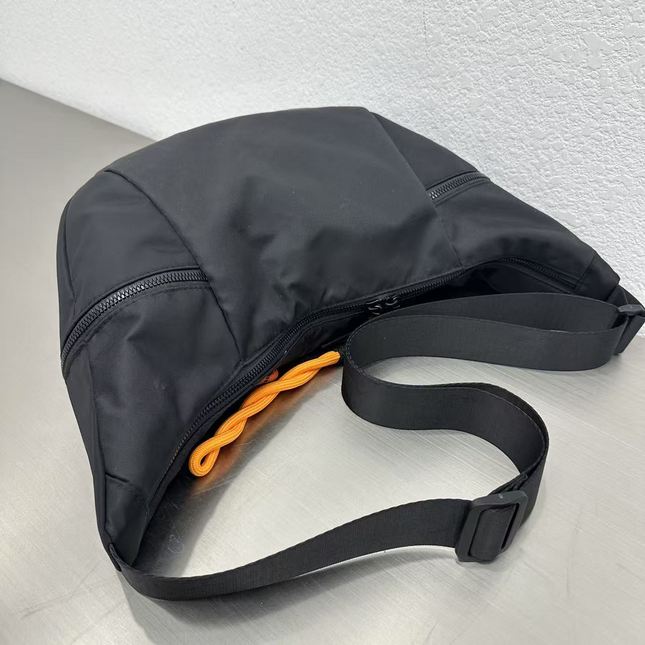 Black bag with a black strap on a light gray backgroundWaterproof tote bag with a durable exterior and a bright orange interior. Features an adjustable strap and multiple pockets for organization. Ideal for travel, gym, or daily use in India.