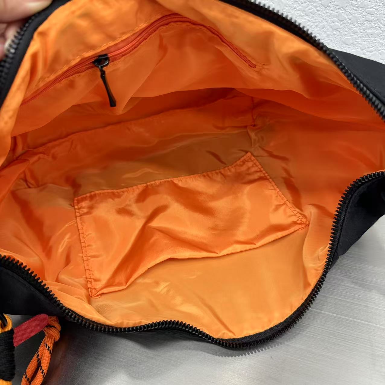 Open orange bag with black zipper on a gray surface Waterproof tote bag with a durable exterior and a bright orange interior. Features an adjustable strap and multiple pockets for organization. Ideal for travel, gym, or daily use in India.