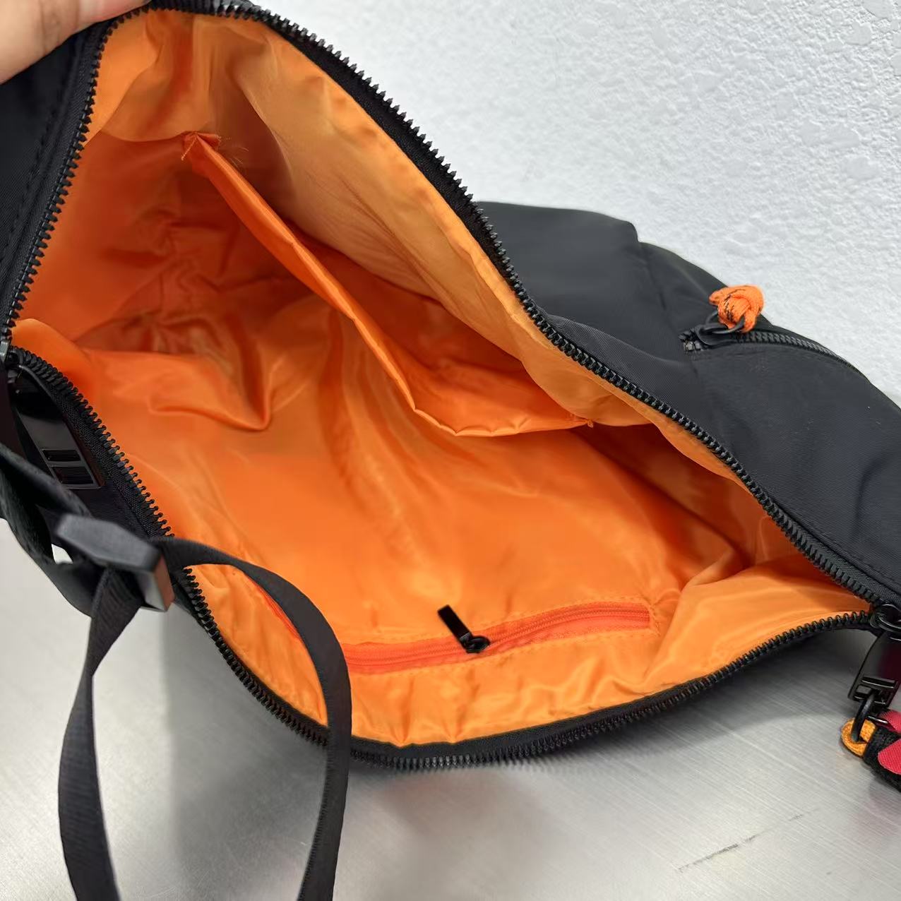 Black bag with orange interior on a light gray background.Waterproof tote bag with a durable exterior and a bright orange interior. Features an adjustable strap and multiple pockets for organization. Ideal for travel, gym, or daily use in India.