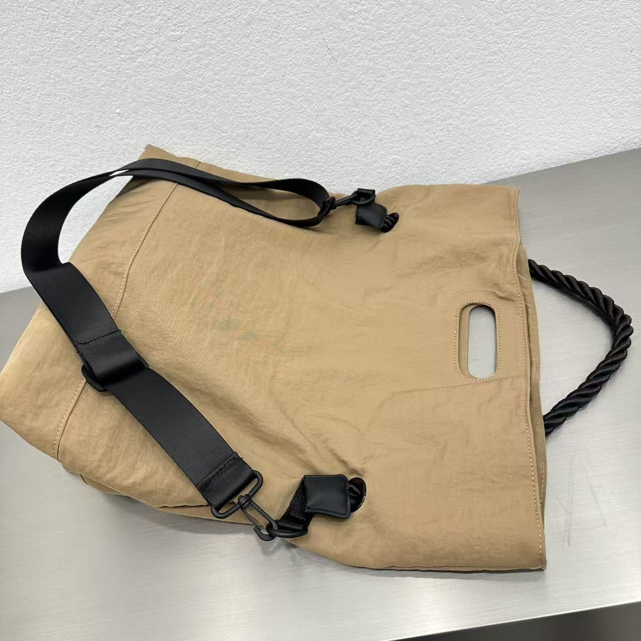 Beige bag with black strap on a light gray surface,High-quality red tote bag for women and girls from a new Indian fashion brand. Features a unique top-fold flap design and sturdy braided black rope handles. Perfect for carrying laptops and essentials, making it a stylish and functional bag for office, college, or casual outings in India. A chic and trending design for the modern Indian woman, available online with free shipping.