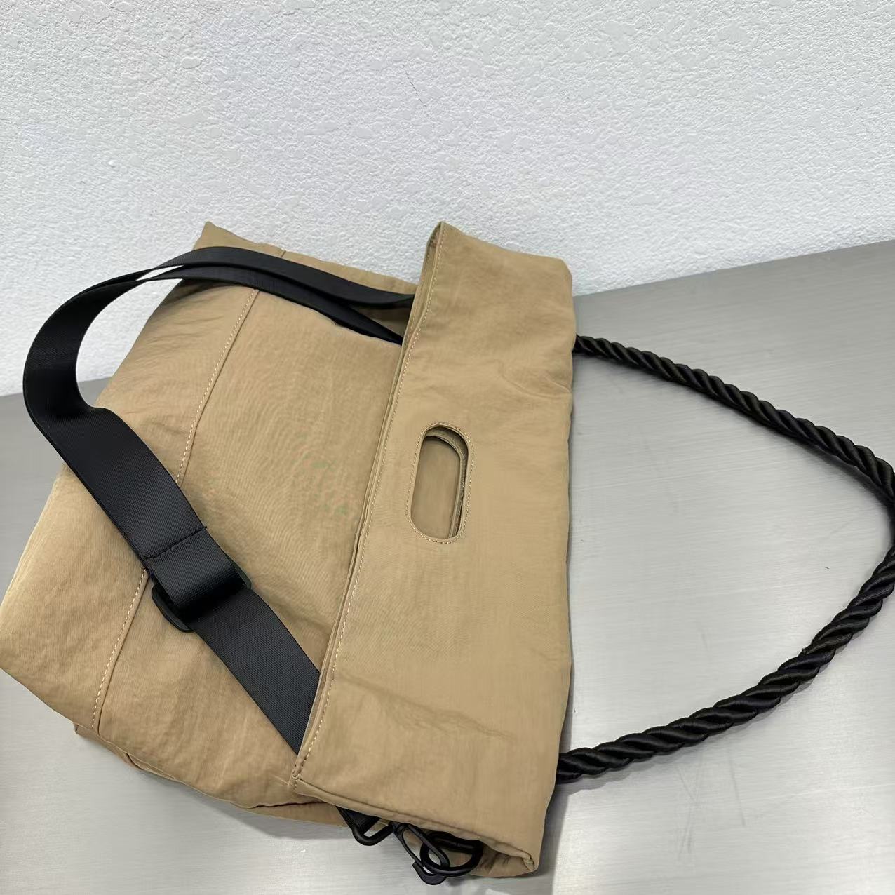 Beige bag with black strap and handle on a light gray background,High-quality red tote bag for women and girls from a new Indian fashion brand. Features a unique top-fold flap design and sturdy braided black rope handles. Perfect for carrying laptops and essentials, making it a stylish and functional bag for office, college, or casual outings in India. A chic and trending design for the modern Indian woman, available online with free shipping.