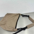 Beige sling bag with black straps on a light gray surface,Convertible nylon tote bag with detachable crossbody strap, zippered front pocket, and main compartment. Available in olive green, black, and beige.