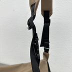 Close-up of a beige bag with black straps on a light gray background,Convertible nylon tote bag with detachable crossbody strap, zippered front pocket, and main compartment. Available in olive green, black, and beige.