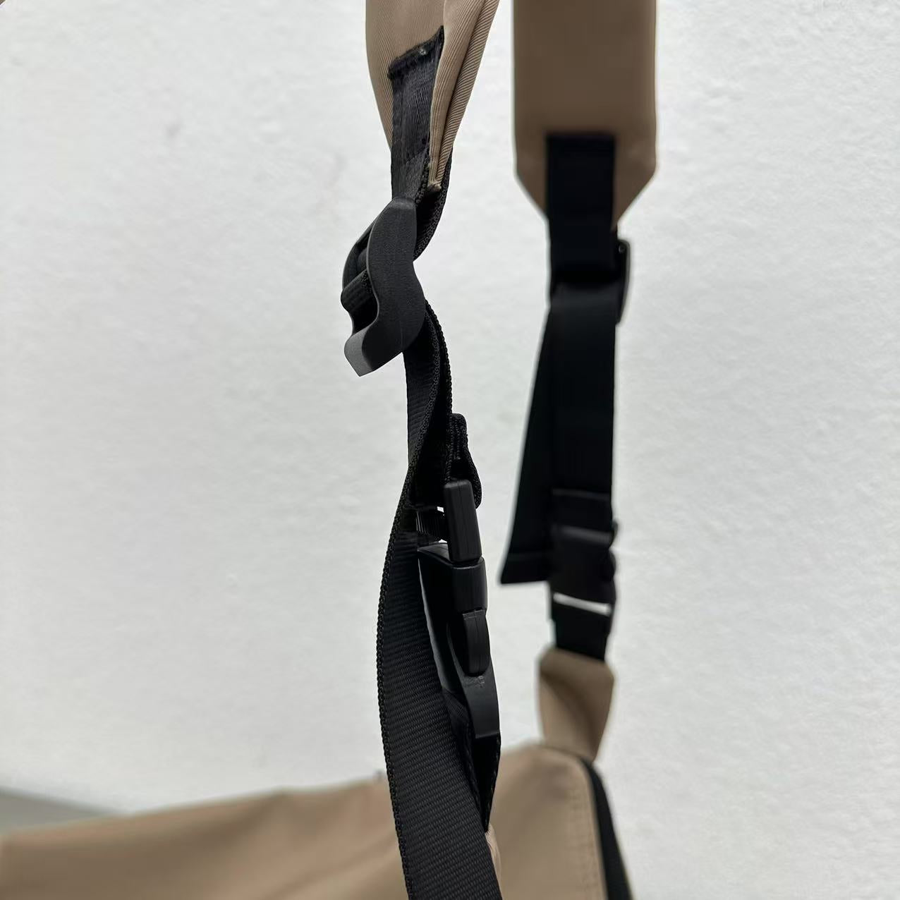 Close-up of a beige bag with black straps on a light gray background,Convertible nylon tote bag with detachable crossbody strap, zippered front pocket, and main compartment. Available in olive green, black, and beige.