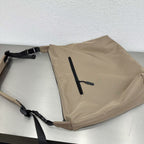 Beige bag with a black strap on a light gray surface,Convertible nylon tote bag with detachable crossbody strap, zippered front pocket, and main compartment. Available in olive green, black, and beige.